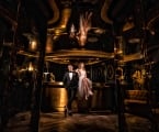 bride and groom sit on a bar in dimly lit room with a golden hue